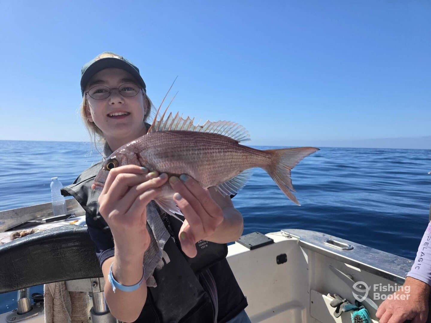 A young angler proudly displaying a Snapper while fishing on a calm day at sea.