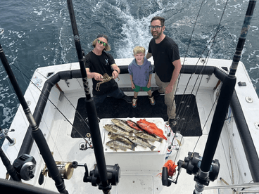 A family enjoys a successful fishing trip, showcasing their catch including various fish and a crab on the boat.