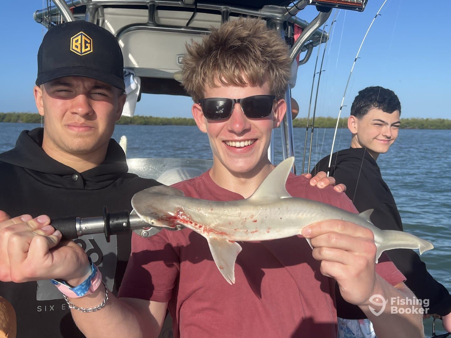Young anglers proudly displaying a small shark while fishing in a scenic coastal environment.