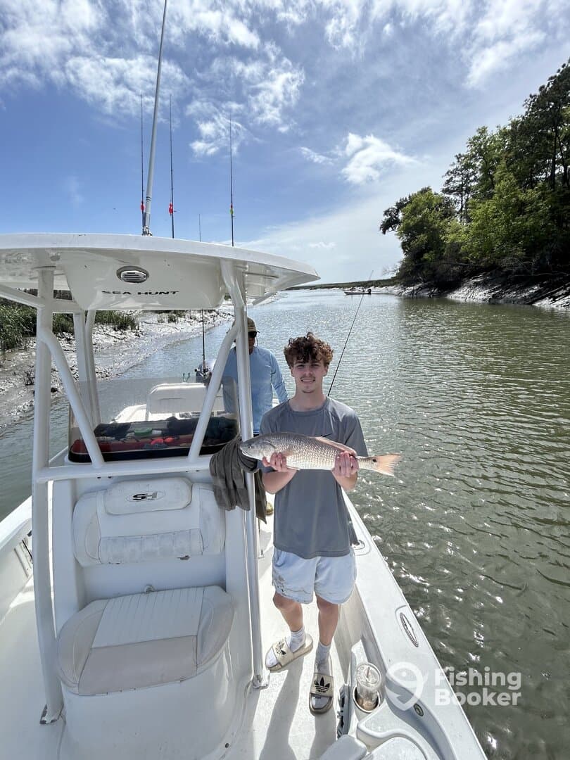 A young angler proudly displaying a Redfish while fishing on a Sea Hunt boat in a scenic waterway.