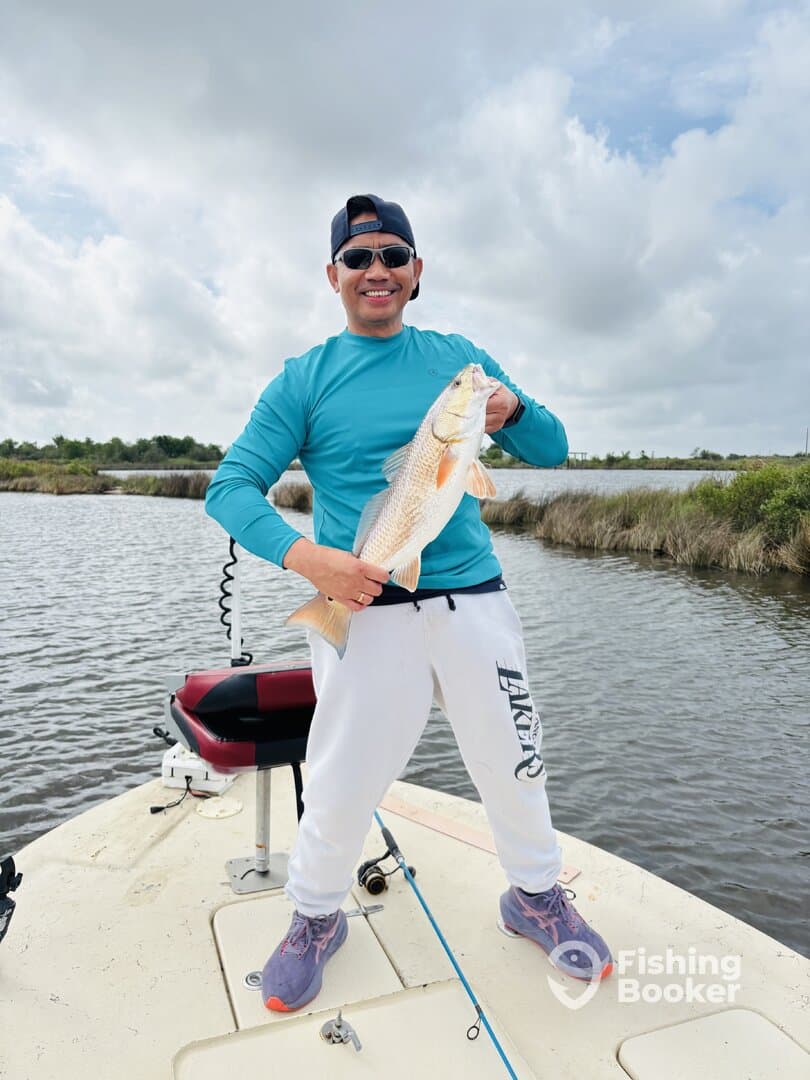 Angler proudly displaying a Redfish while fishing from a boat in a scenic waterway.