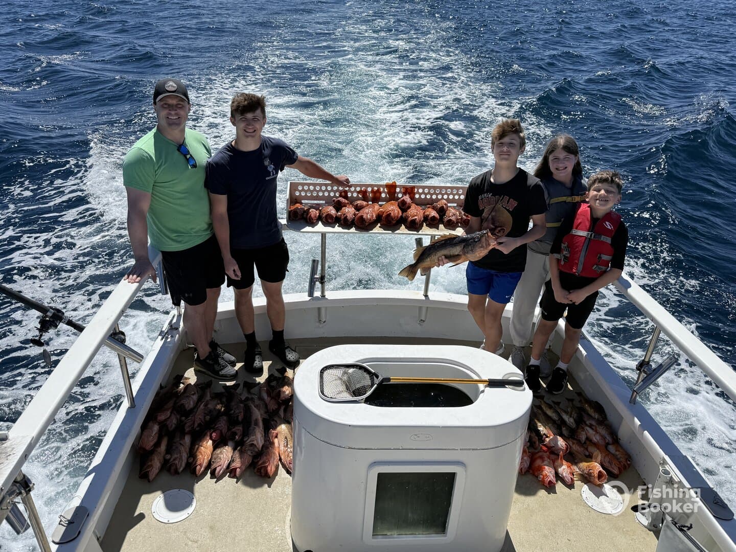 A family group proudly displays their catch of Red Snapper and other species aboard a fishing boat, showcasing a successful day on the water.