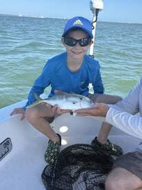 A young angler proudly displaying a small fish while fishing on a boat, showcasing a fun day on the water.