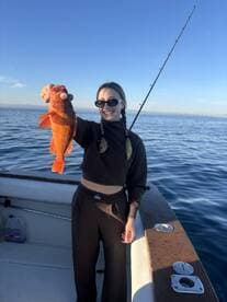 A young woman proudly displaying a vibrant orange rockfish while fishing on a sunny day.