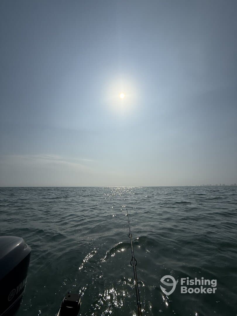 A serene view of the ocean with a fishing rod in the foreground, capturing the sun's reflection on the water.
