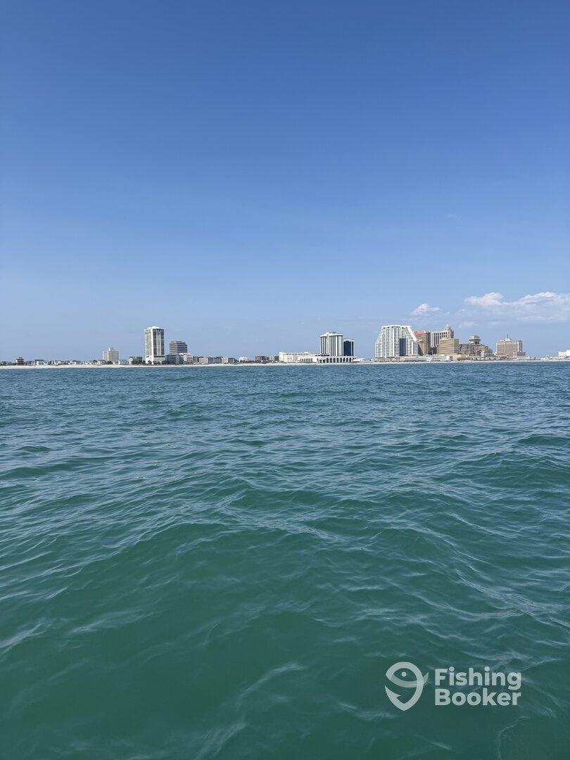 A scenic view of the coastline with high-rise buildings under a clear blue sky, taken from a boat on the water.
