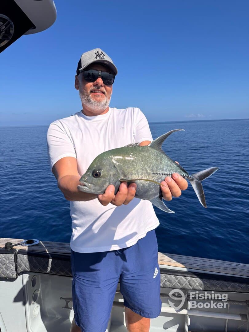 Angler proudly displaying a Grey Snapper while fishing in clear blue waters.