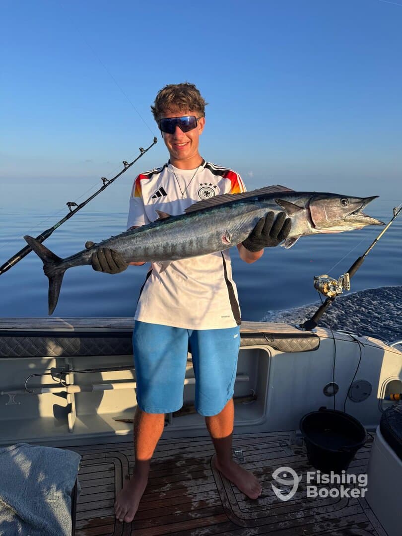 Young angler proudly holding a large Wahoo on a fishing charter, showcasing a successful day on the water.