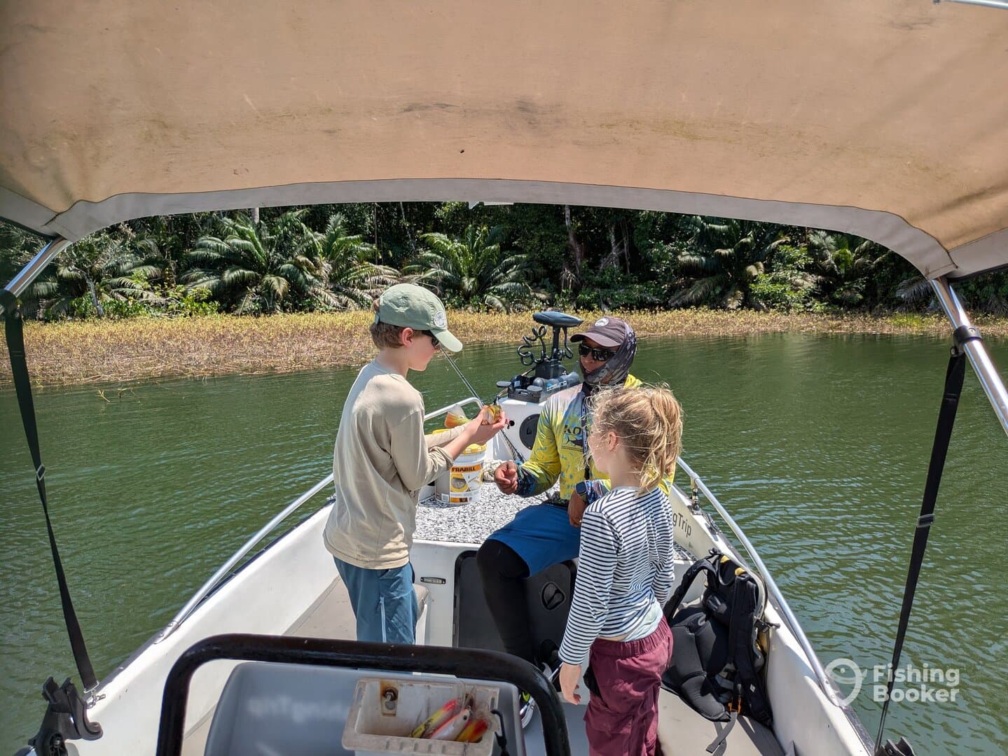 Two children engaged in fishing activities with an instructor on a boat in a lush, tropical environment.