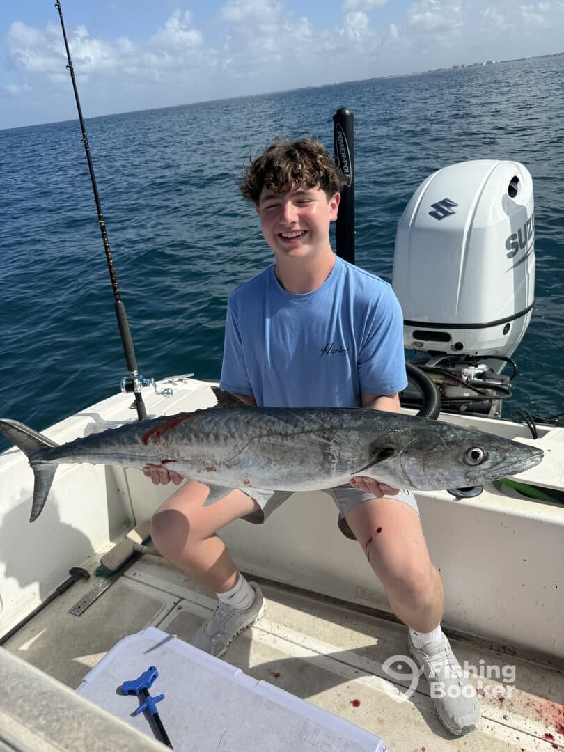 Young angler proudly holding a large King Mackerel aboard a fishing boat, showcasing a successful day on the water.
