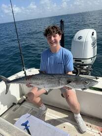 Young angler proudly holding a large King Mackerel aboard a fishing boat, showcasing a successful day on the water.