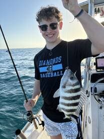 A young angler proudly displaying a striped fish while fishing on a boat, enjoying a sunny day on the water.