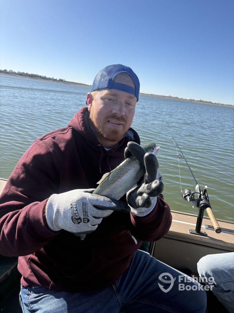 Angler holding a Rainbow Trout while fishing on a calm lake, showcasing a successful catch during a relaxing day on the water.