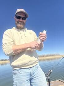 Angler proudly displaying a freshly caught Rainbow Trout while fishing on a calm lake.