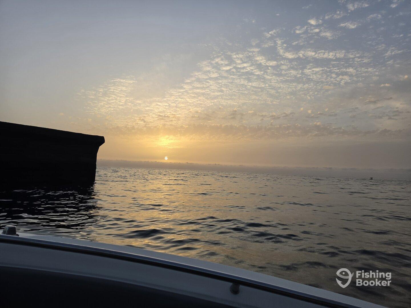 A serene sunrise over the water, captured from the side of a boat, showcasing the calm fishing environment.