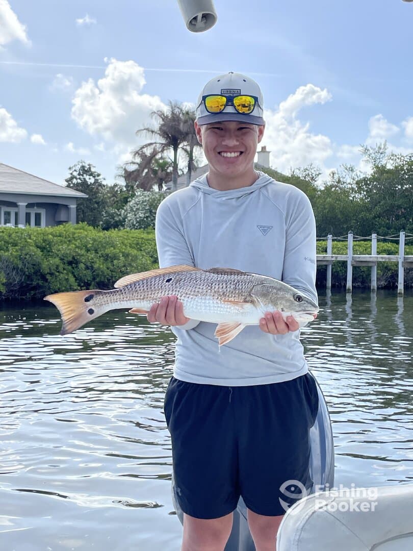 A young angler proudly displaying a Redfish while fishing near the shore, showcasing a beautiful day on the water.