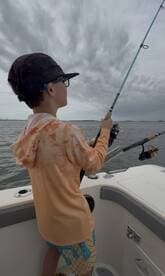 A young angler casting a line while fishing on a boat, surrounded by a cloudy sky.