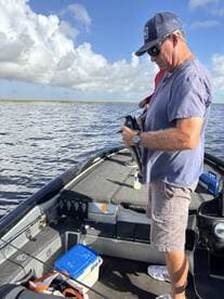 An angler focused on reeling in a fish while fishing from a boat in a scenic waterway, showcasing a relaxed fishing environment.