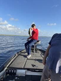 Angler proudly displaying a large Bass while fishing from a boat in a serene waterway.
