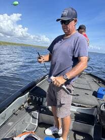 Angler actively reeling in a fish while fishing from a boat in a scenic waterway, showcasing a vibrant fishing environment.