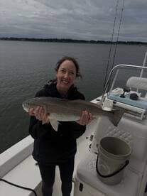 A happy angler proudly displaying a large Redfish while on a fishing boat, showcasing a successful catch in a serene water setting.