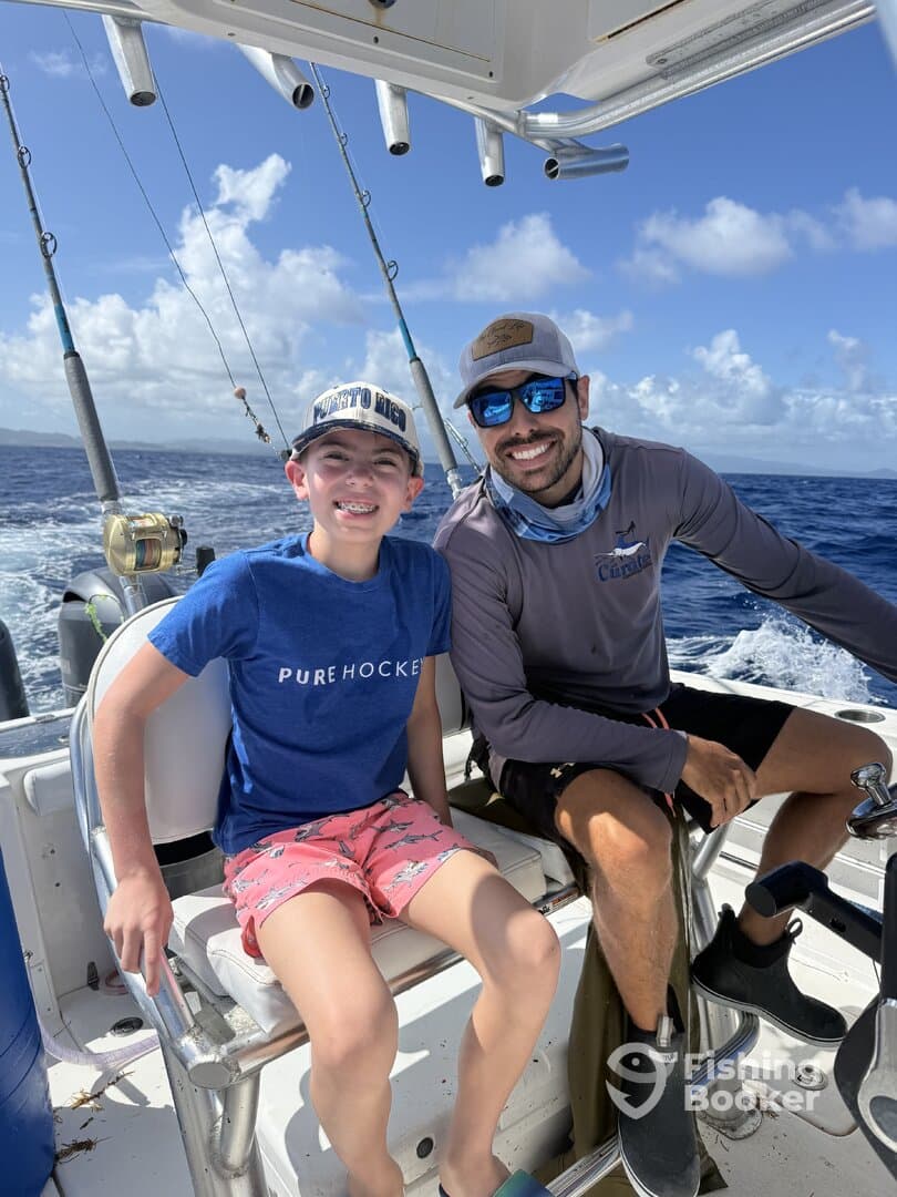 A young boy and an adult enjoying a fishing trip on a boat, showcasing the interior seating and a beautiful ocean backdrop.
