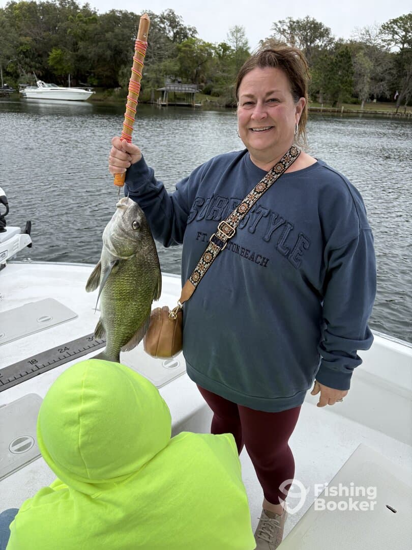 A proud angler displaying a large fish while enjoying a fishing trip on a calm waterway, accompanied by a child in a bright hoodie.