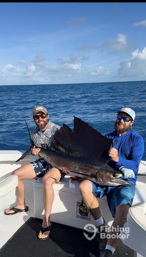 Two anglers proudly displaying a large Sailfish on a fishing charter in clear blue waters.