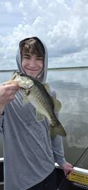 A young angler proudly displaying a large Largemouth Bass while fishing on a calm lake.