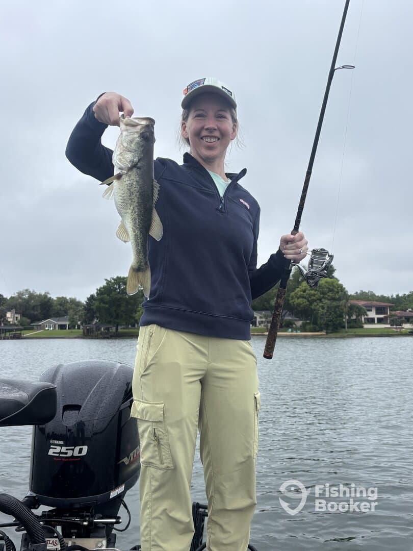 Angler proudly displaying a large Largemouth Bass while fishing from a boat on a calm lake.