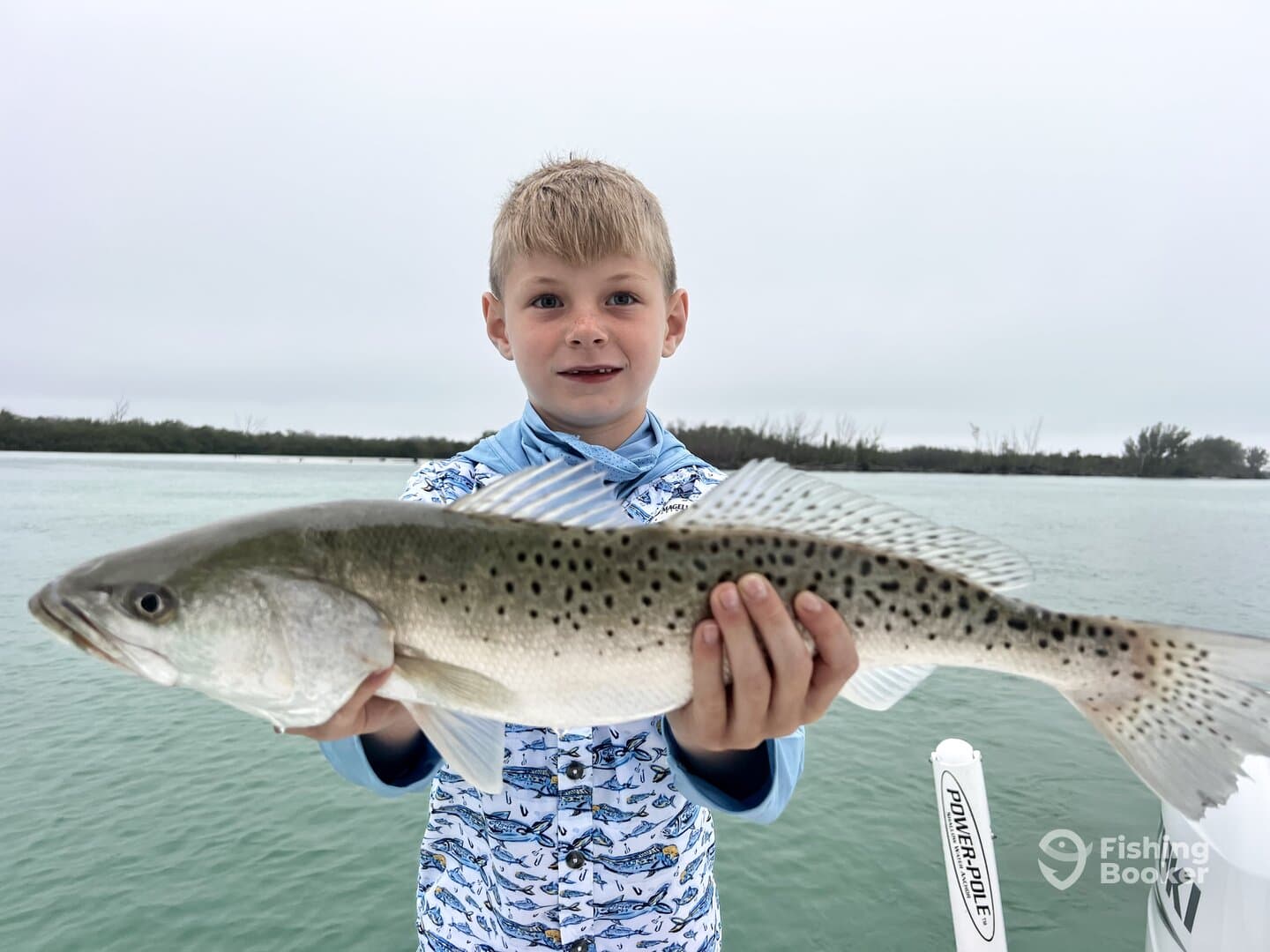 Young angler proudly holding a large Speckled Trout while fishing in a coastal waterway.