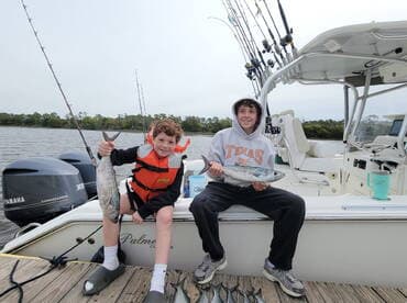 Two young anglers proudly displaying their catches aboard a fishing boat, showcasing a successful day on the water.