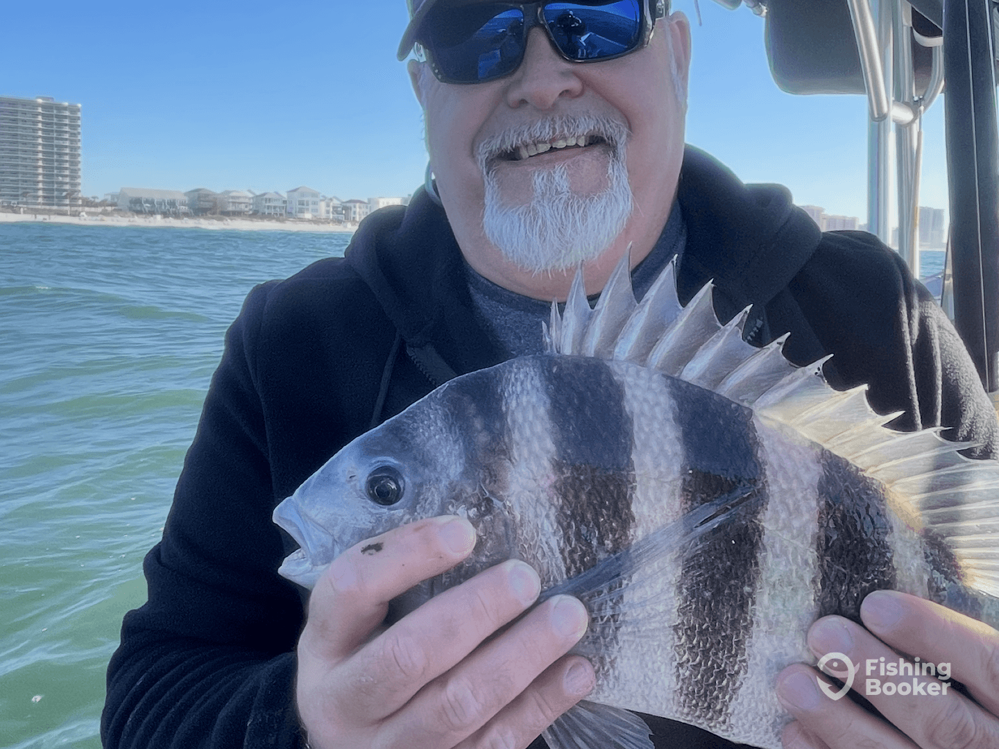 Angler proudly displaying a Sheepshead caught while fishing near the shore, with a scenic backdrop of coastal buildings.