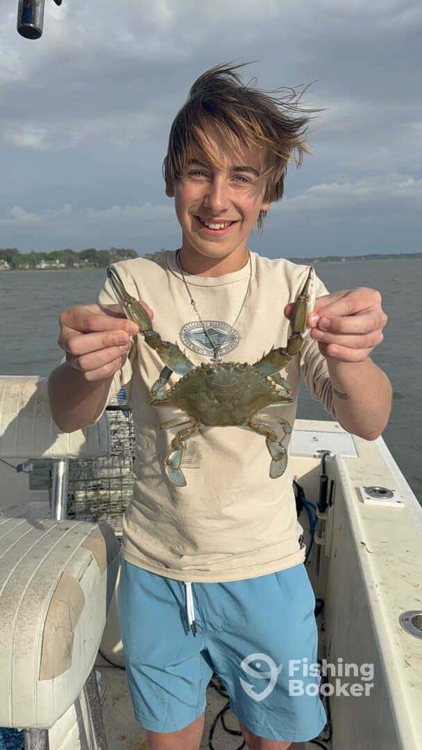 A young angler proudly displaying a large blue crab while fishing on a boat, showcasing a fun day on the water.