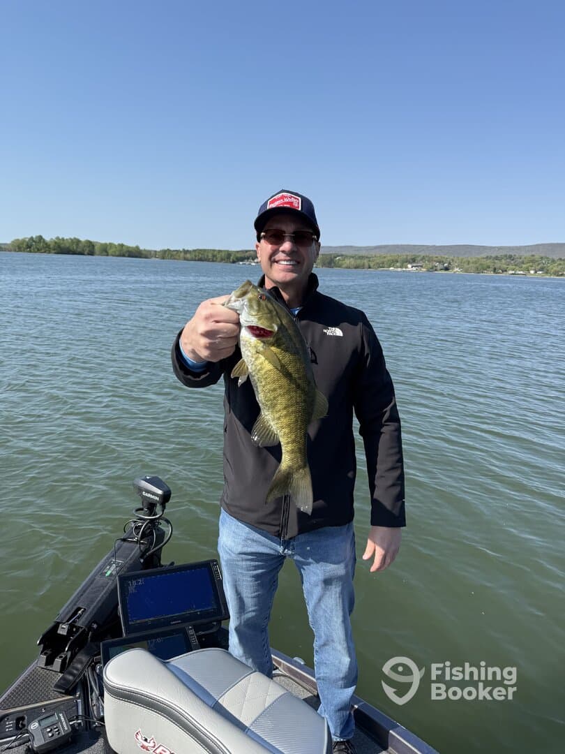 Angler proudly displaying a large Largemouth Bass while fishing from a boat on a clear day.