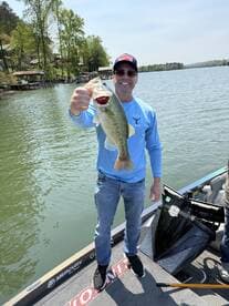 An angler proudly displaying a large Largemouth Bass while fishing on a serene lake, showcasing a beautiful spring day.
