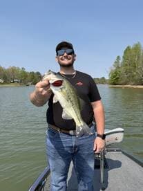 Angler proudly displaying a large Largemouth Bass while fishing on a serene lake, showcasing a beautiful day outdoors.