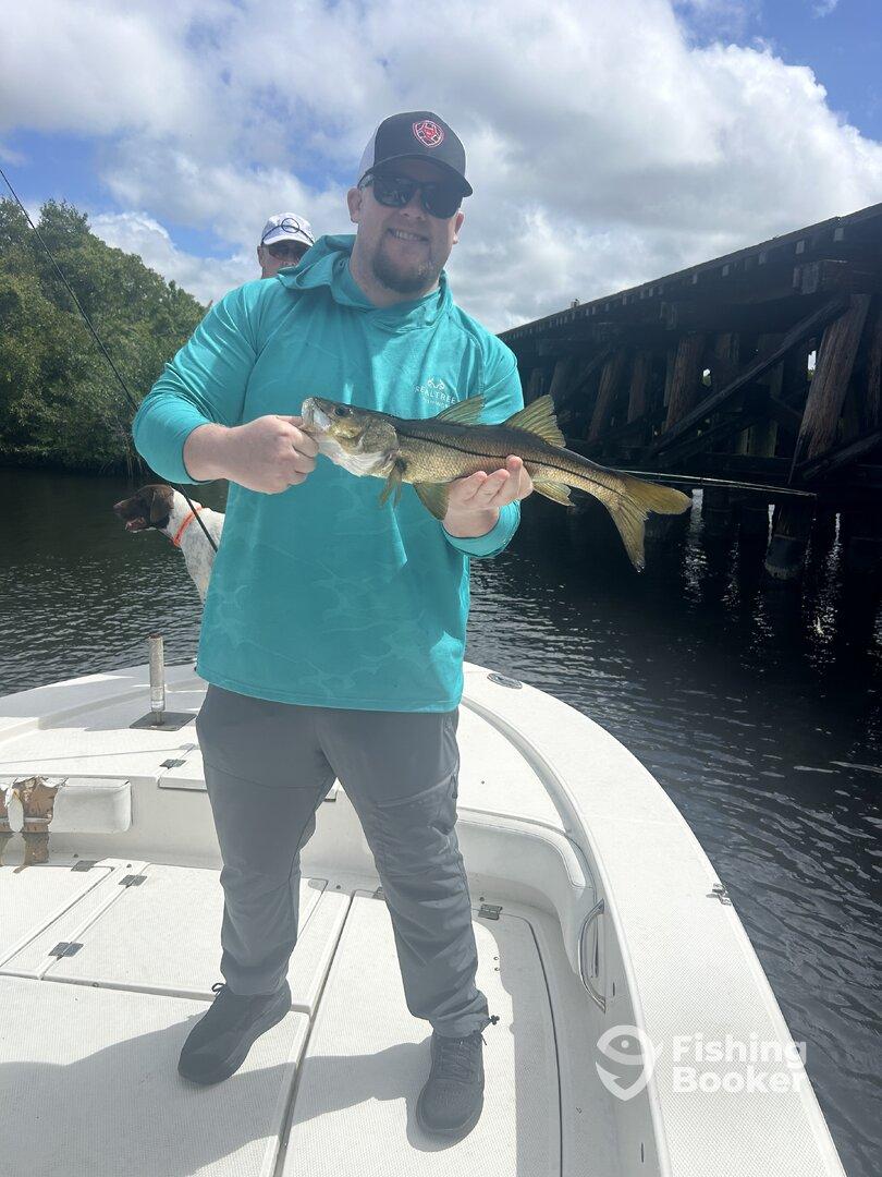 Angler proudly displaying a Snook caught while fishing from a boat in a scenic waterway.