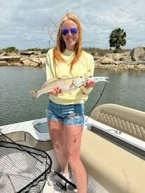 A proud angler holding a Redfish while standing on a boat in a scenic fishing environment.