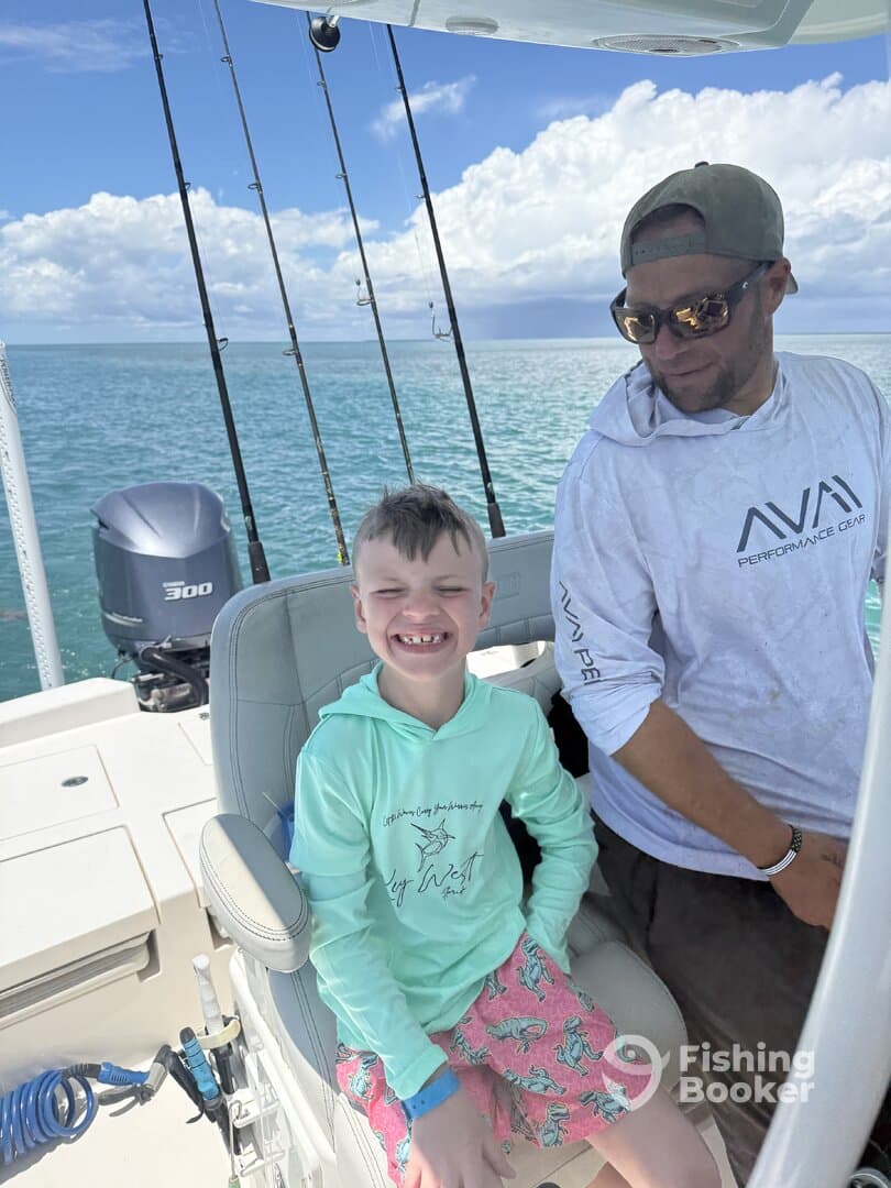 A young boy and an adult are enjoying their time on a fishing boat, with the ocean in the background, showcasing a fun day out on the water.