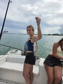 A young angler proudly displaying her catch, a striped bass, while fishing on a boat in calm waters.