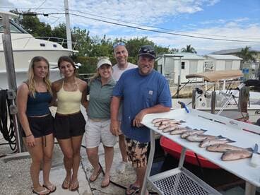 A group of four anglers proudly posing with their catch of Snapper displayed on a cleaning table at the dock.