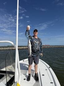 Angler proudly displaying a Speckled Trout while standing on the bow of a boat in a coastal fishing environment.