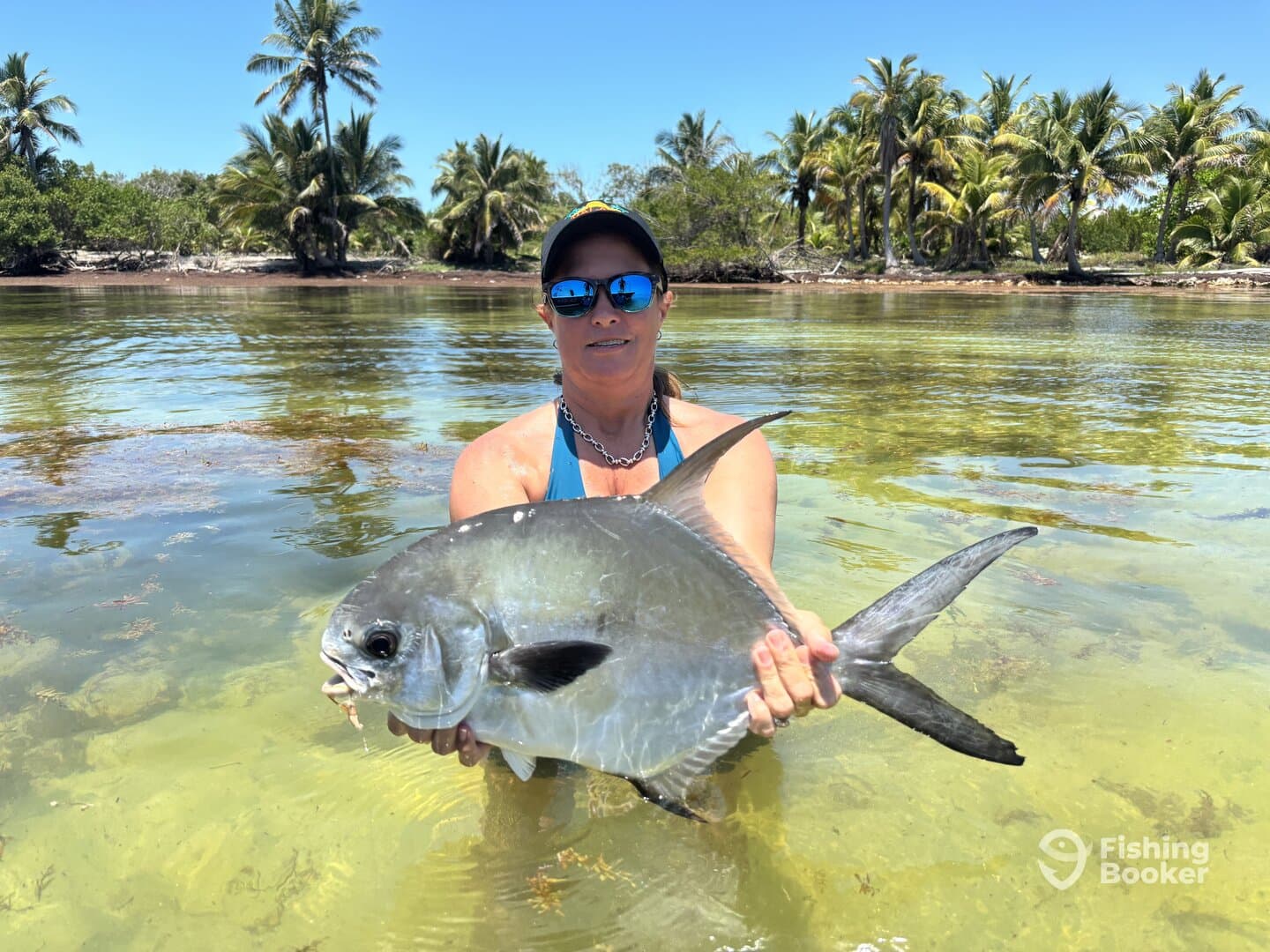 Angler proudly displaying a large Permit in shallow waters surrounded by palm trees, showcasing a vibrant fishing environment.