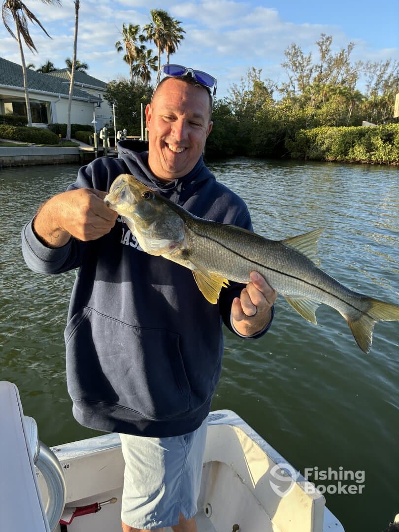 Angler proudly displaying a Snook caught while fishing from a boat in a scenic waterway.