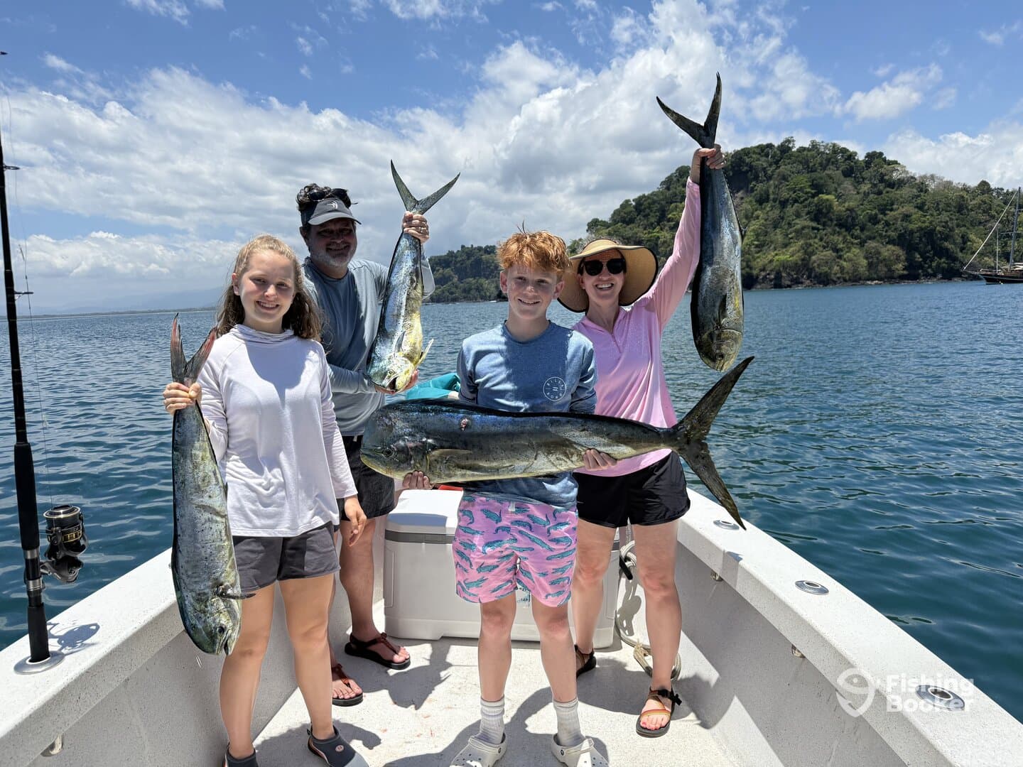 A family proudly displaying their catch of Mahi Mahi on a sunny day aboard a fishing boat.