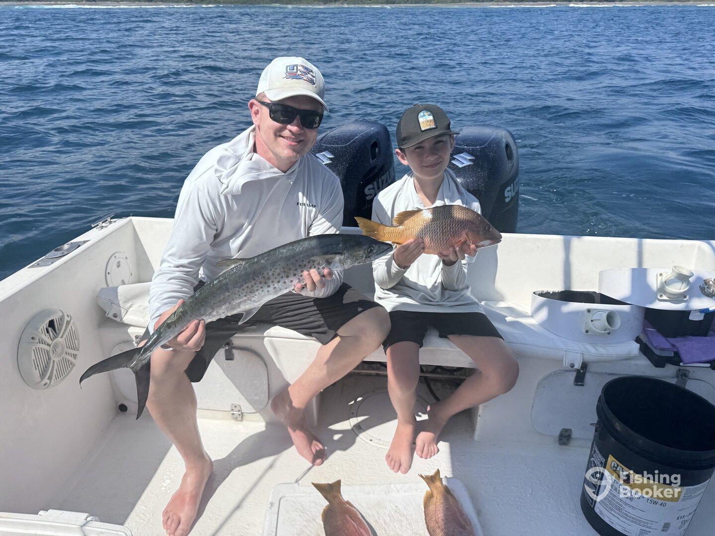 A proud father and son duo displaying their catch, featuring a large King Mackerel and a Snapper, while enjoying a day of fishing on the open water.