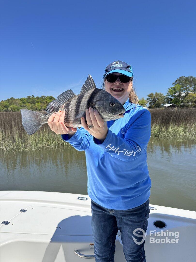 A young angler proudly displaying a striped black drum while fishing from a boat in a scenic coastal environment.