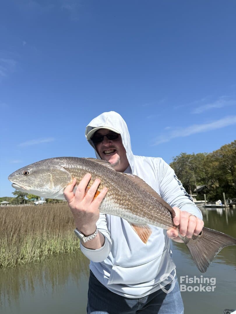 Angler proudly displaying a large Redfish while fishing in a scenic coastal environment.