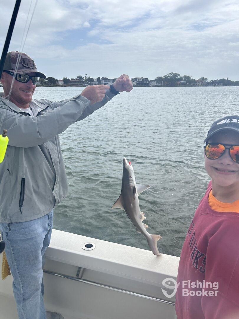 A young angler smiles as a shark is being reeled in during a fishing trip, showcasing the excitement of the catch.